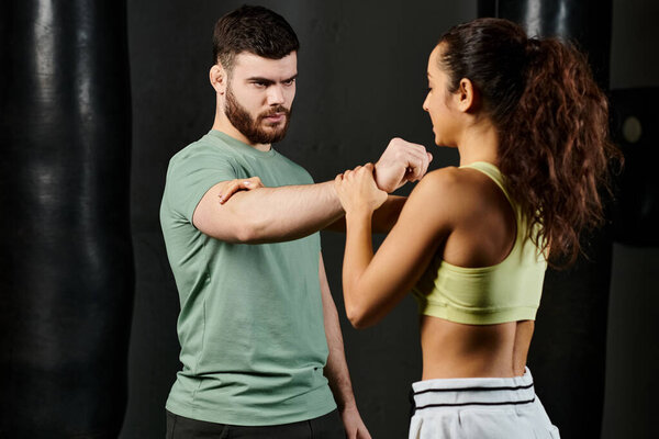 A male trainer teaches self-defense techniques to a woman in a gym setting.