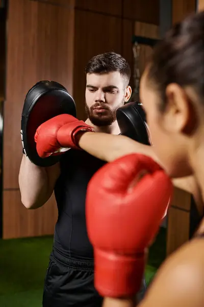 stock image A woman in a black shirt and red boxing gloves trains in a gym.