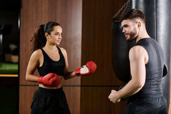 A male trainer is coaching a brunette sportswoman in boxing gloves in a gym setting.