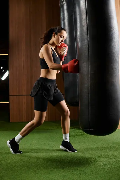 stock image A brunette sportswoman in black shorts fiercely boxing with a red glove in a gym.