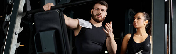 A personal trainer assists a brunette sportswoman in front of a gym machine.