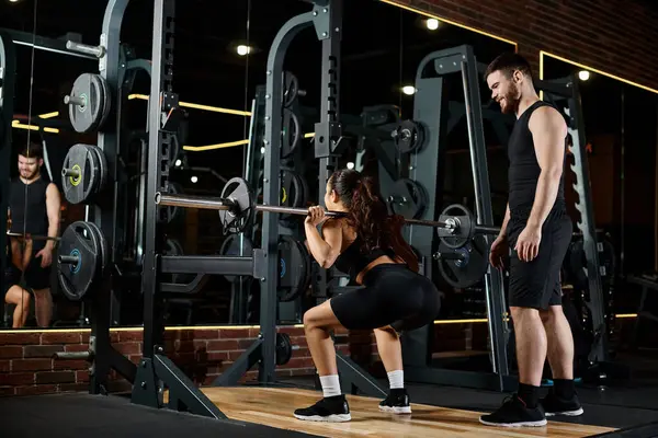 stock image A personal trainer and a brunette sportswoman synchronously perform squats in a well-equipped gym.