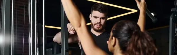 stock image A male trainer stands alongside a brunette sportswoman as they observe themselves in a gym mirror.