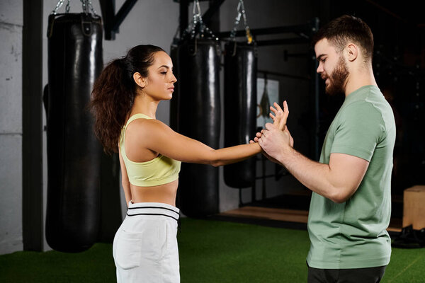 A male trainer demonstrates self-defense techniques to a woman in a gym, showcasing empowerment and teamwork.