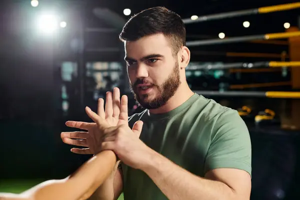 stock image A man demonstrates self-defense techniques to a woman in a gym setting in front of a camera.