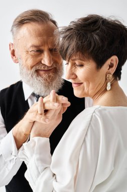 Düğün kıyafetleri içinde orta yaşlı bir gelin ve damat stüdyo ortamında neşeyle kucaklaşır..