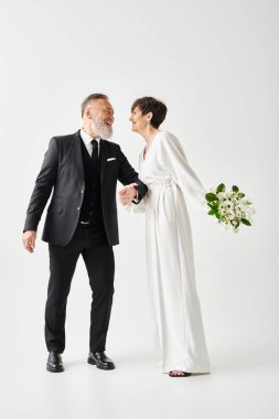 Siyah beyaz düğün kıyafetleri içinde orta yaşlı gelin ve damat stüdyo ortamında özel günlerini kutluyorlar..