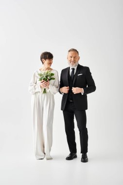 Resmi giysiler içinde orta yaşlı gelin ve damat bir stüdyoda birlikte özel günlerini sevgi ve zarafetle kutluyorlar..