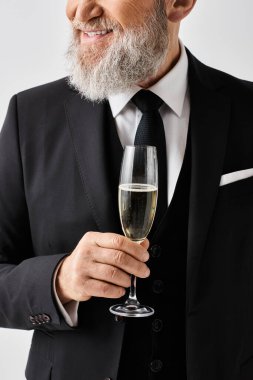 Şık takım elbiseli orta yaşlı bir damat zarif bir şekilde elinde şampanya kadehi tutuyor, düğün gününde sofistike ve klas bir hava yayıyor..