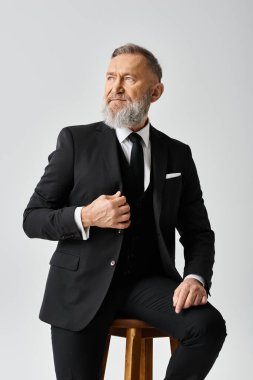 Şık bir takım elbise giymiş orta yaşlı bir damat düğün gününde stüdyo sandalyesinde zarifçe oturur..