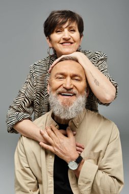 Orta yaşlı bir adam, şık bir stüdyo ortamında bir kadını destekliyor, gücünü ve güvenini gösteriyor..