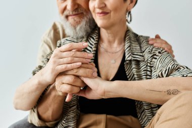 A middle-aged man and woman, in stylish attire, sit closely together in a serene studio setting, displaying a strong connection. clipart