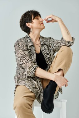 A stylish middle-aged woman with short hair sits gracefully atop a pristine white stool in a chic studio setting. clipart