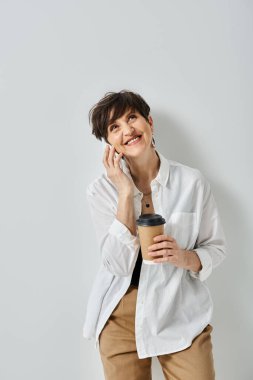 Kısa saçlı orta yaşlı bir kadın, şık giyinmiş, elinde bir fincan kahve tutarak ve cep telefonuyla sohbet ederek birden fazla iş yapıyor..