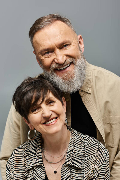 A middle aged man and woman in fashionable attire posing affectionately for a camera in a studio setting.