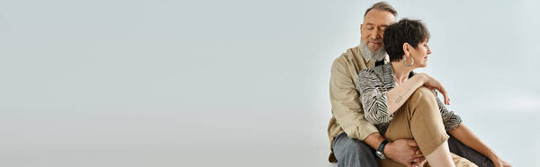 Мужчина и женщина средних лет в стильной одежде выражают любовь, крепко обнимая друг друга.