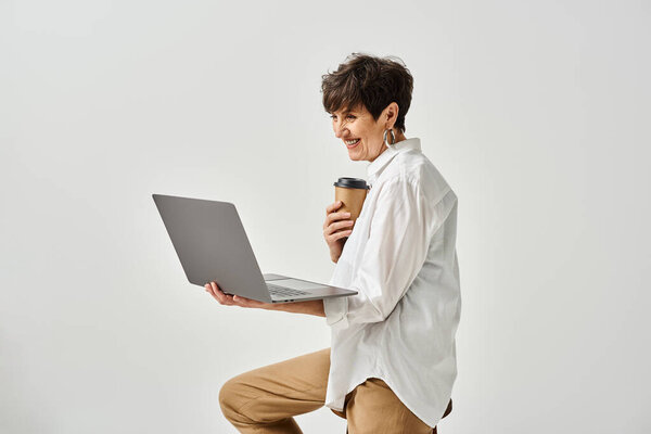 Женщина средних лет, сидящая на стуле, держащая ноутбук в стильной студии.