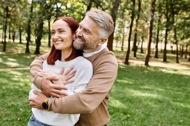 A man affectionately hugs a woman in a park setting. clipart