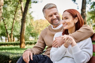 Bir erkek ve bir kadın, sevgi dolu bir çift, parktaki bankta huzur içinde oturur..