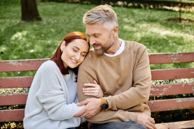 A man and a woman in casual attire sitting together on a park bench. clipart