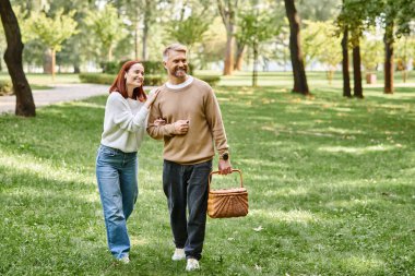 A man and a woman in casual attire walking peacefully through a park. clipart