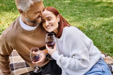 Bir adam ve bir kadın parkta bir battaniyenin üzerinde şarabın tadını çıkarıyorlar..