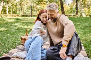 Bir adam ve bir kadın parkta bir battaniyeye oturup birlikte huzurlu bir anın tadını çıkarıyorlar..