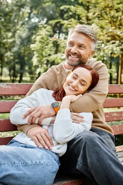 Bir adam ve bir kadın günlük giysiler içinde parkta bir bankta oturup birlikte huzurlu bir anın tadını çıkarıyorlar..