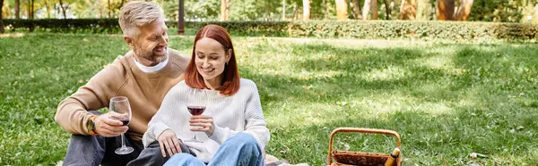 stock image Adult man and woman sitting on a blanket, holding wine glasses in a park.