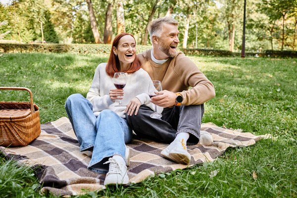 A man and woman relax on a blanket in a grassy park.