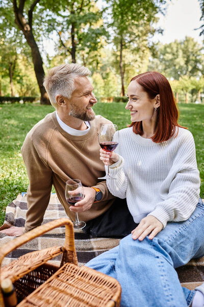 Man and woman enjoying wine on a blanket in the park.