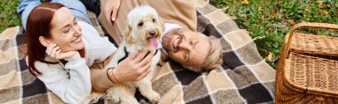 A couple relaxes on a blanket with their dog in a peaceful park setting. clipart