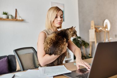 Kısa saçlı sakin bir kadın bir masada otururken, kedi kucağında dinleniyor, evde birlikte geçirdiğimiz değerli anın tadını çıkarıyor..