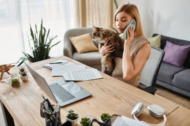 A stylish woman chatting on a cellphone while snuggling her adorable cat at home. clipart