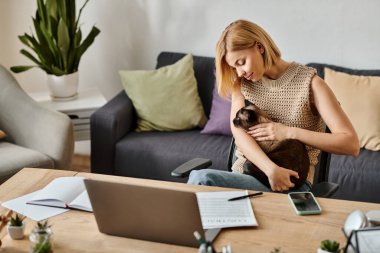 Kısa saçlı bir kadın kanepeye oturur, kucağında küçük bir kedi, bir anlık bağ ve arkadaşlığın tadını çıkarır..
