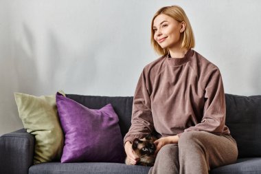 Kısa saçlı bir kadın kanepede oturmuş kedisiyle bağ kuruyor..