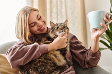 Kısa saçlı bir kadın kanepede oturuyor, kedisini sakin bir ifadeyle tutuyor..