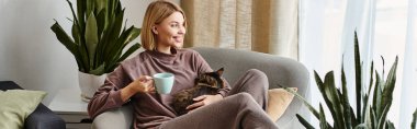 A woman with short hair sits in a chair, holding a cup while her cat curiously snuggles close. clipart