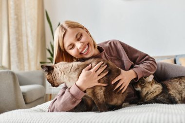Kısa saçlı, çekici bir kadın. Yatakta uyuyor. Yanında da iki oyuncu kedi var..