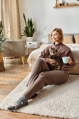 A tranquil moment as a woman with short hair sits on a bed, tenderly holding her cats paw. clipart