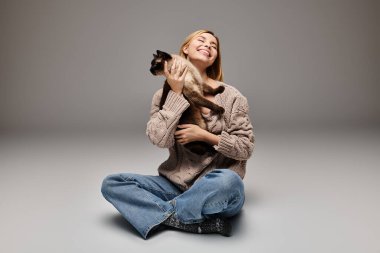 Kısa saçlı bir kadın evinde huzurlu bir arkadaşlık anında kedisini kucaklayarak yerde oturuyor..