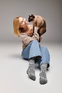 Kısa saçlı şık bir kadın yerde oturuyor, kedisi omuzlarına tünemiş..