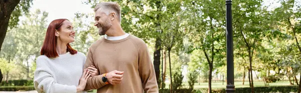 stock image A loving adult couple in casual attire walking together through a serene park.