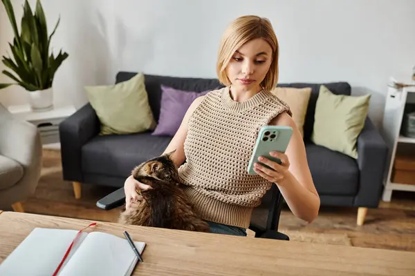 stock image A short-haired woman sits at a table with her cat, scrolling on her cell phone, enjoying a moment of relaxation at home.