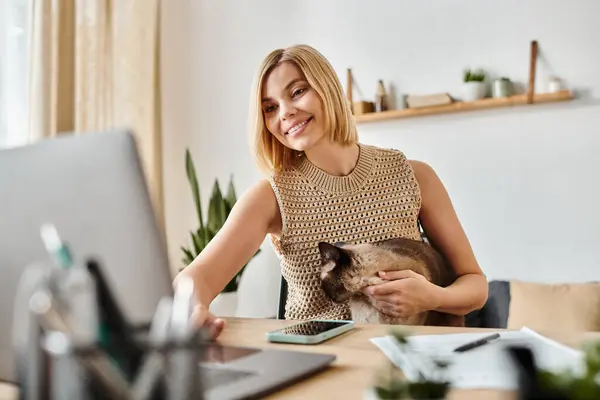 一个留着短发的女人坐在办公桌前 专心致志地在笔记本电脑里 而她的猫却坐在她身边 营造出一种宁静的氛围 — 图库照片