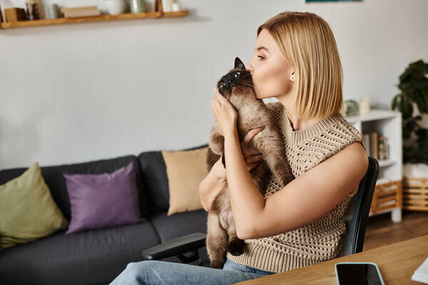 Женщина с короткими волосами расслабляется за столом, нежно держа кошку дома.