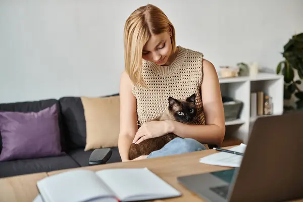 一位矮发的心满意足的女人坐在桌旁 她的猫在她的腿上 在家里享受着宁静的时光 — 图库照片