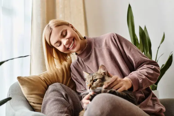 stock image A stylish woman with short hair sitting on a couch, gently petting her content cat.