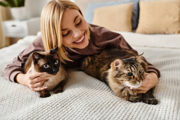 A woman with short hair peacefully lays on a bed, surrounded by two cats, enjoying a moment of tranquility at home.
