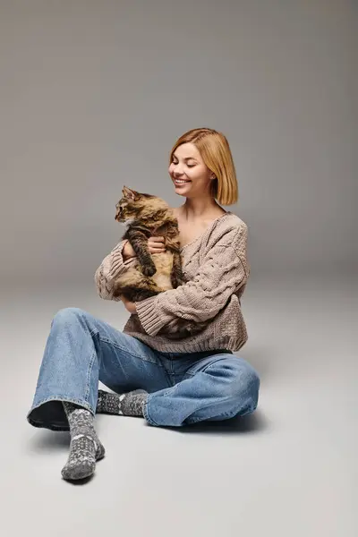 床に座っている短い髪の女性は 穏やかに自宅で平和で親密な瞬間に猫を抱いています — ストック写真